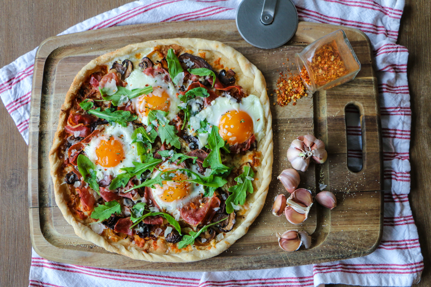 Breakfast pizza with arugula, soft bakes eggs, caramelized onions, and prosciutto